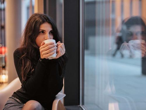 a woman sitting down drinking a cup of coffee at ibis Nürnberg Hauptbahnhof in Nürnberg
