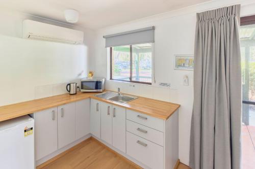a kitchen with white cabinets and a sink and a window at RAC Busselton Holiday Park in Busselton