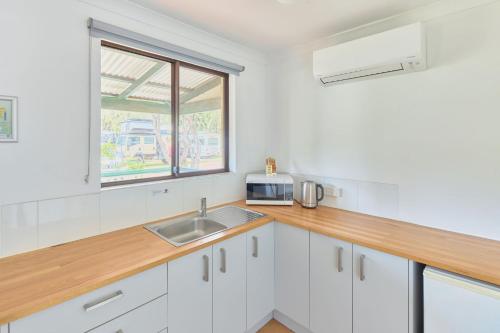 a kitchen with white cabinets and a sink and a window at RAC Busselton Holiday Park in Busselton