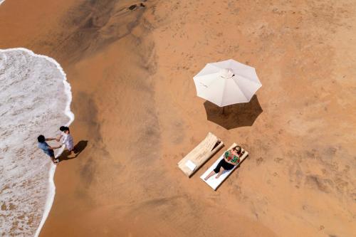two people sitting on a beach with an umbrella at EZHIMALA AYURVEDA AND WELLNESS RESORT in Payyannūr