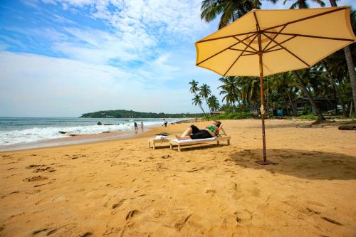 a woman sitting on a chair under an umbrella on the beach at EZHIMALA AYURVEDA AND WELLNESS RESORT in Payyannūr