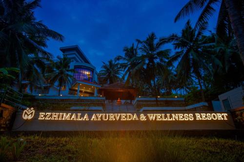 a sign in front of a building with palm trees at EZHIMALA AYURVEDA AND WELLNESS RESORT in Payyannūr