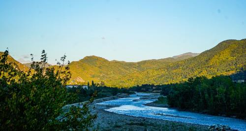 a river with trees and mountains in the background at Kvabtkari Cottages in Ambrolauri