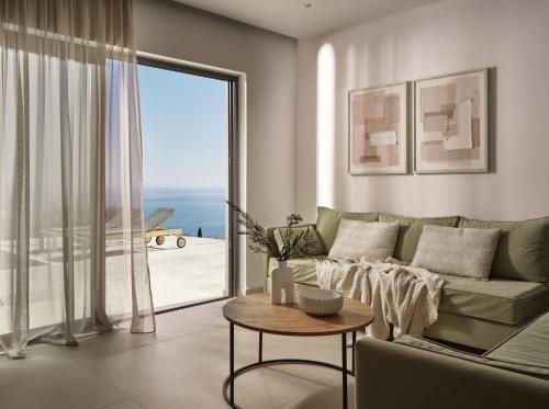 a living room with a couch and a large window at Askos Luxury Suites, a Zakynthian Hideaway, By ThinkVilla in Agios Nikolaos