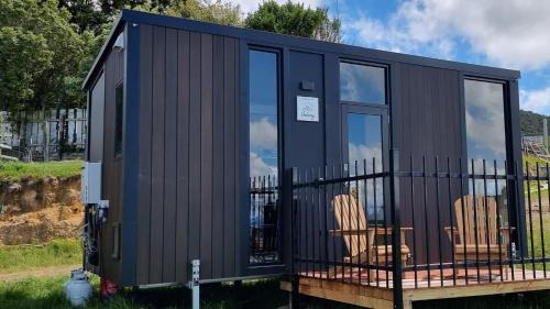 a black tiny house with two chairs on a deck at Aorangi Peak Cabins 5 by Tiny Away in Rotorua