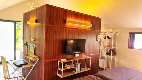 a bedroom with a wooden wall with a flat screen tv at Adachi Farmstay Bảo Lộc in Bao Loc