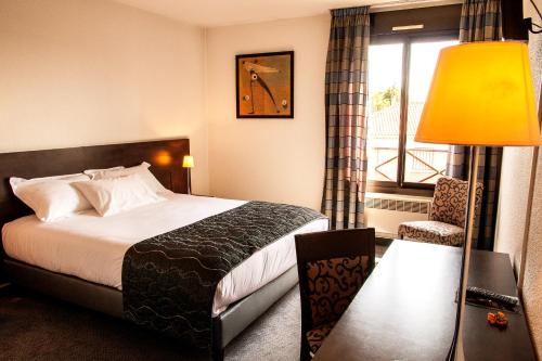 a hotel room with a bed and a chair and a window at Hotel Les Amandiers in Tournon-sur-Rhône