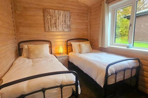 two beds in a room with wooden walls and two windows at Heather Lodge with Hot Tub in Holcombe Burnell
