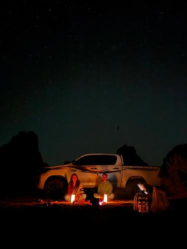 two people sitting in front of a car at night at Rum Angel Camp in Wadi Rum