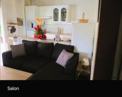 a living room with a black couch and a kitchen at Villa Ti Gîte - Piscine privée in Le Marin