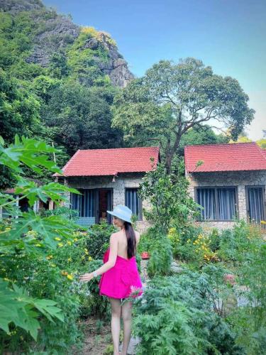 a woman in a pink dress walking through a garden at Trang an green river homestay in Ninh Binh