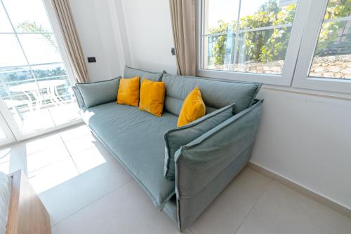 a green couch with yellow pillows in a room with windows at Kotarja Apartments in Dhërmi