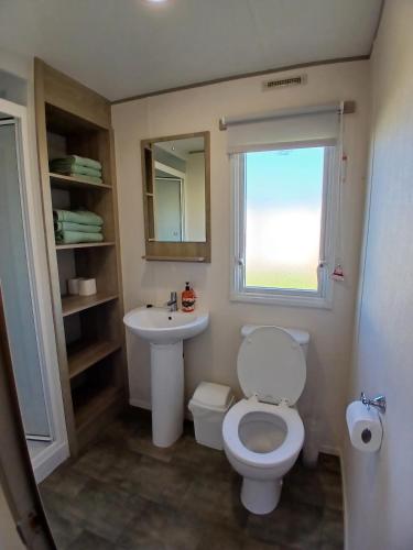 a bathroom with a toilet and a sink and a window at Gold Plus Caravan in Dymchurch