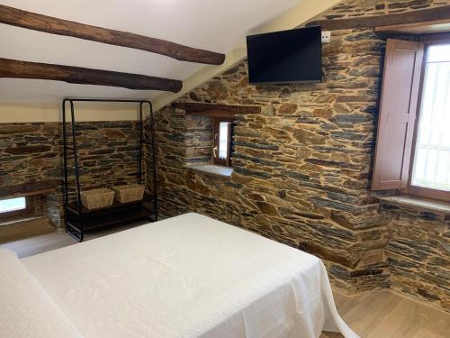 a bedroom with a stone wall with a bed and a tv at Apartamentos Casa Benito in San Tirso de Abres