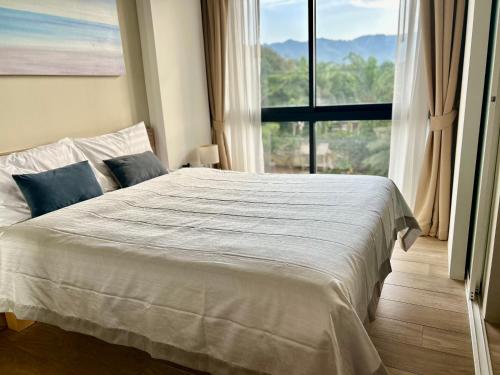 a bedroom with a white bed with a large window at Modern Condo at Diamond Resort in Bang Tao Beach
