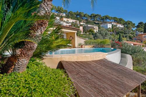 une piscine avec un banc en bois à côté d'un palmier dans l'établissement Somptueuse Villa l'Oasis By HC, à Carqueiranne