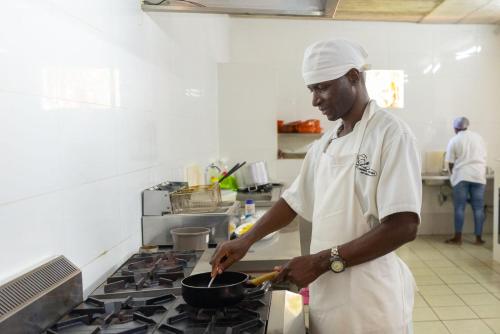 a man in a kitchen preparing food in a pan at Telvina Beach Lodge in Vilanculos