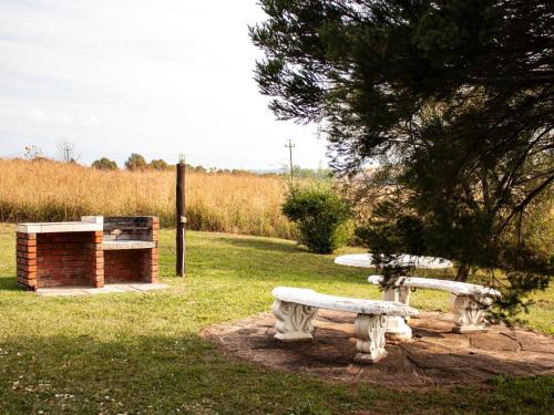 two white benches sitting in a park with a fireplace at Tranquility Farmstays in Winterton