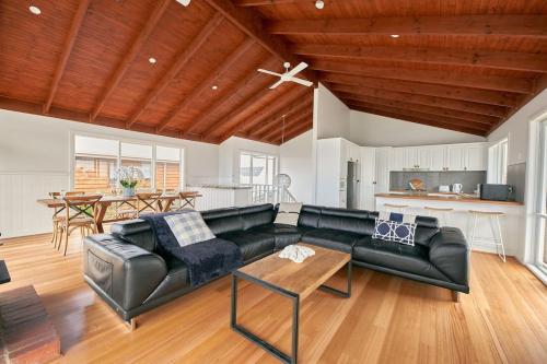 a living room with a black leather couch and a kitchen at The Palm House 200 meters to the beach in Torquay