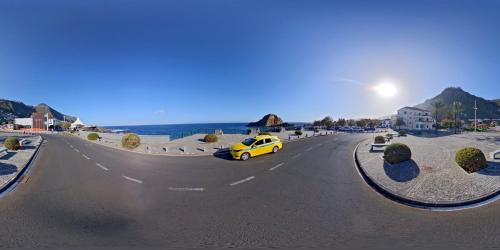 a yellow car driving down a road next to the ocean at Pensão Fernandes in Porto Moniz