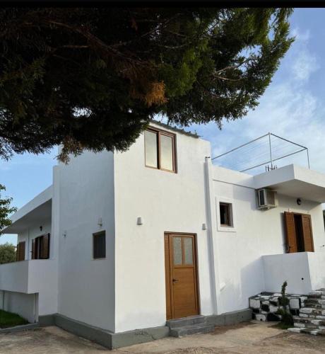 a white house with a wooden door and a tree at VILA GOLDEN SAND in Ksamil