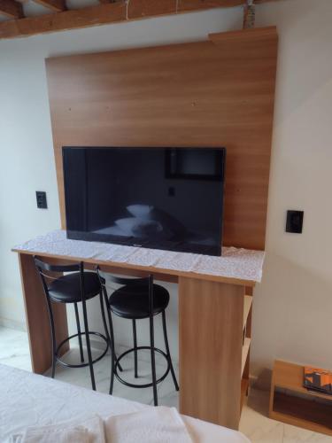 a kitchen with a bar with two stools and a tv at Loft aconchegante in Ilhota