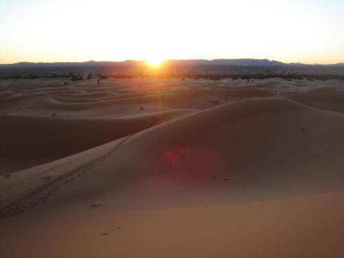a desert with the sun setting in the horizon at Riad Dar Poublanc in Merzouga