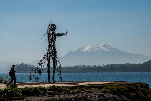 a man walking past a statue of a person with a mountain in the background at Acogedor Departamento en Zona Residencial in Puerto Varas