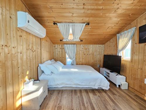 a bedroom with a white bed and a television at Jeju Nova Pension in Jeju