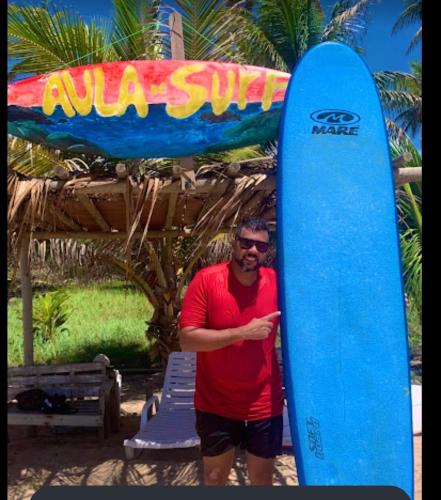 a man standing in front of a blue surfboard at Pousada Luar da Praia in Imbassai