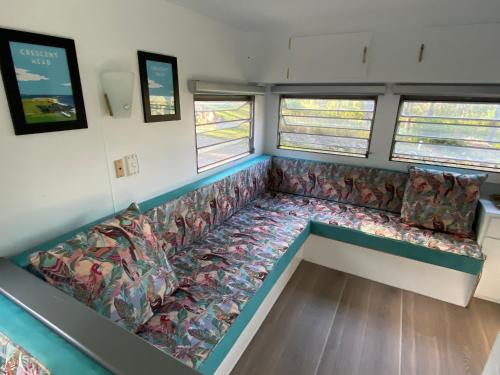a couch in the middle of a room with windows at Alice & Elvis, Crescent Head, Retro Caravans with Deck, Bathroom & Outdoor Bath in a Bush Setting near the Beach in Crescent Head