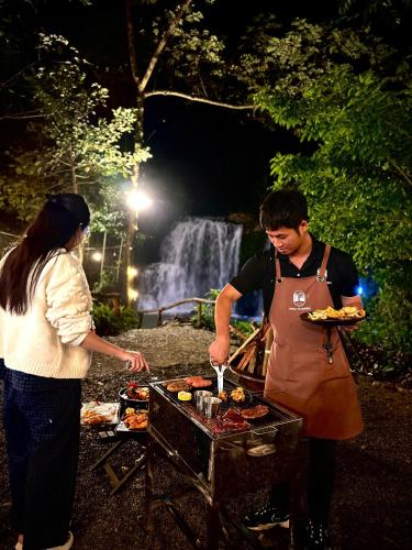 a man and a woman preparing food on a grill at Zenda Glamping in Bao Loc