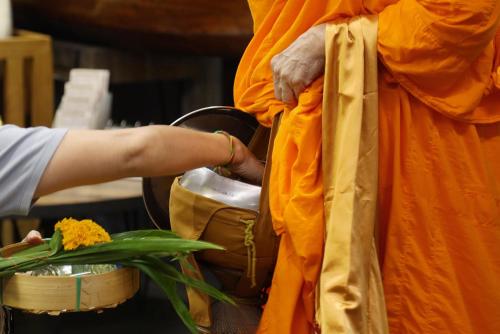 a person wearing an orange robe is putting flowers in a pot at Amphawa Nanon Hotel in Amphawa