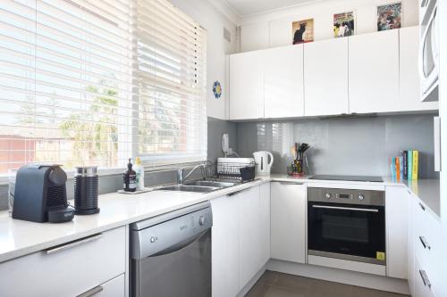 a white kitchen with a sink and a dishwasher at Beach Side Getaway - Brighton Le-Sands 2 Bedroom Apartment in Sydney