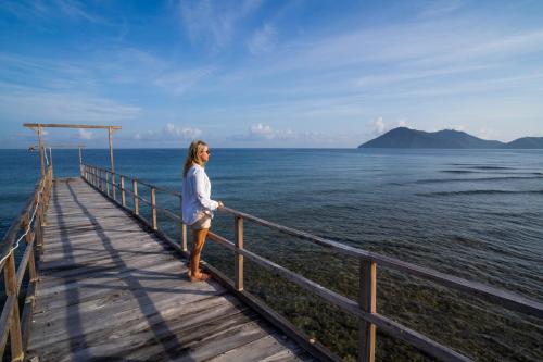 Eine Frau steht auf einem Holzsteg über dem Wasser in der Unterkunft Sofanda Resort & Dive in Nangamiro