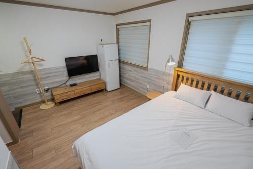 a bedroom with a white bed and a flat screen tv at Daecheon sagwanamu pension in Boryeong