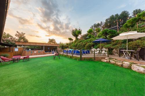 a yard with a green lawn with umbrellas and chairs at Gapyeong Petmily Dog Pension in Gapyeong