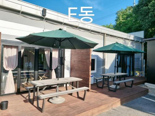 two picnic tables and two umbrellas on a deck at Forest Caravan Pension Incheon in Incheon