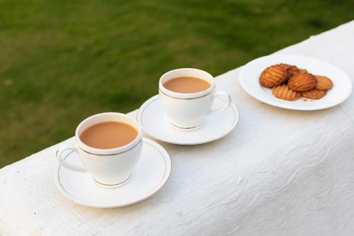 two cups of coffee and a plate of cookies on a table at StayVista at The Francolin Farm with Free Breakfast, Infinity Pool & Jacuzzi in Sohna
