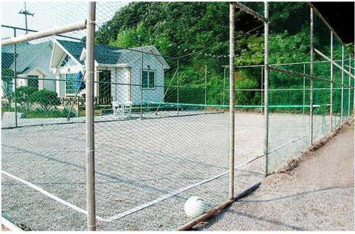 a tennis net on a tennis court with a house at Anmyeondo Lake Park Pension in Ch'anggi-ri