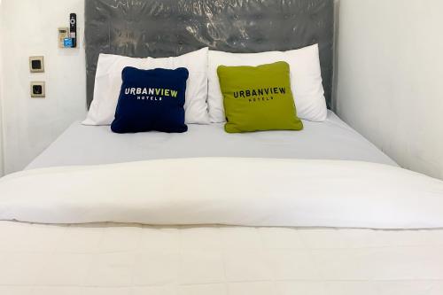 a white bed with two blue and yellow pillows at Urbanview Hotel Permata Syariah Garut in Paledang