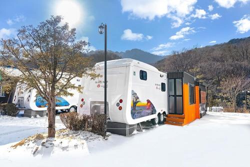 a white trailer parked next to a tree in the snow at Muju camping Caravan in Samgong