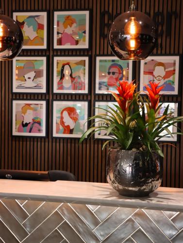 a vase with flowers on a table with pictures on the wall at Garner Hotel Preston Samlesbury by IHG in Preston