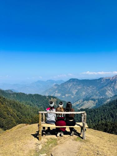 three people sitting on a bench on top of a mountain at The Rustic Jibhi - Backpackers Hostel in Jibhi
