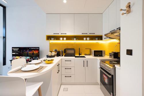 a kitchen with white cabinets and a yellow wall at UrbanHomes - Cozy Spacious Exceptional Studio in Heart of Dubai at JVC in Dubai