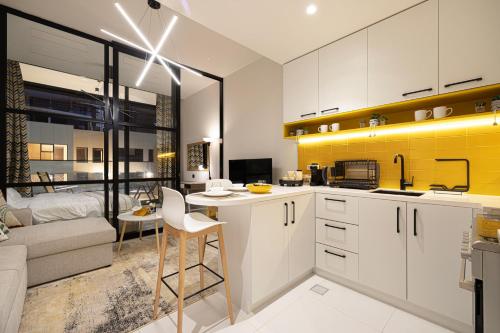 a kitchen with white cabinets and a yellow accent wall at UrbanHomes - Cozy Spacious Exceptional Studio in Heart of Dubai at JVC in Dubai