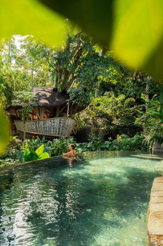 a person in a swimming pool with a house in the background at Ulaman Eco Luxury Resort in Tabanan