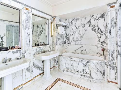 a white bathroom with two sinks and a tub and a mirror at Le Meurice – Dorchester Collection in Paris