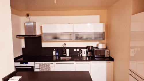 une cuisine avec des armoires blanches et un comptoir noir dans l'établissement Appart cosy tout confort Metro 11 avec parking, à Paris