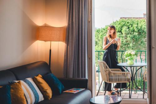 a woman in a black dress standing on a balcony at Le Suffren Hôtel in Grimaud